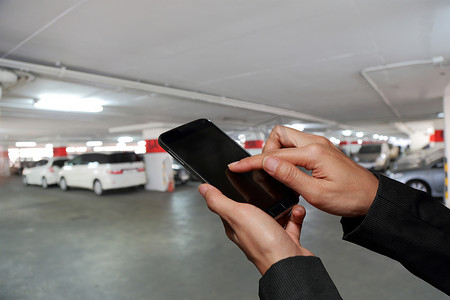 女人手触摸屏智能手机，手机上模糊抽象停车场背景作为地方概念。