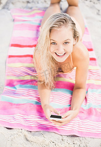 手机夏季夏季摄影照片_快乐的女人躺在沙滩上使用手机