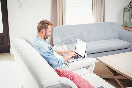 起居室摄影照片_男人坐在客厅的沙发上使用笔记本电脑
