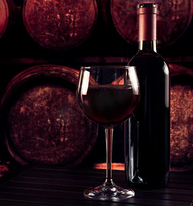 在木桌上和旧酒窖背景中靠近瓶子的红酒杯