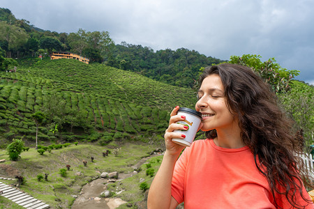 在绿茶谷的背景下，黑发旅游女孩享用工艺杯中的茶。