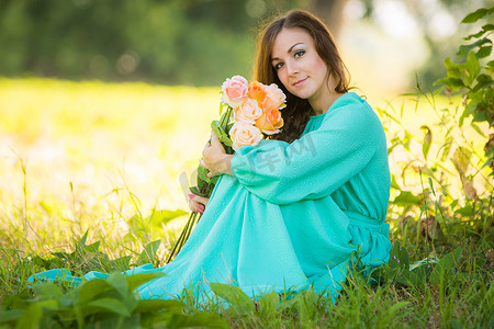 女孩拿鲜花摄影照片_阳光明媚的日子里，一个年轻女孩拿着一束玫瑰坐在树荫下的画像