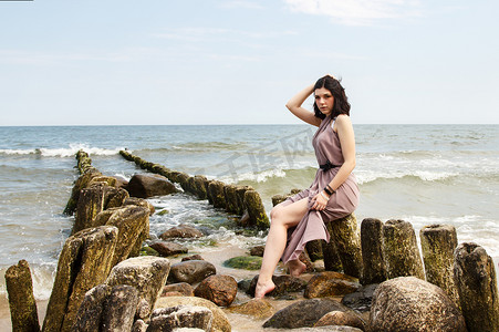 坐在海边防波堤上的米色裙子的年轻黑发女人