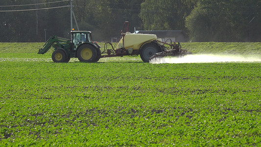 农药喷洒杂草摄影照片_秋季拖拉机喷洒农药化学品的油菜籽田