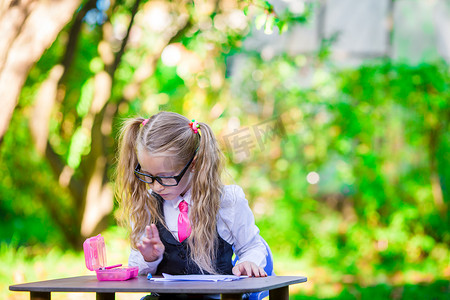 聪明的小女生坐在办公桌前，带着笔记和铅笔在户外。