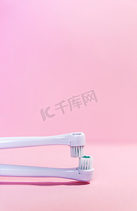 柔和的浅粉色背景中的两把电动牙刷