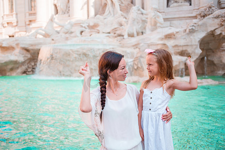 旅行的家庭妈妈和女孩在意大利罗马的特雷维喷泉投掷硬币以求好运。