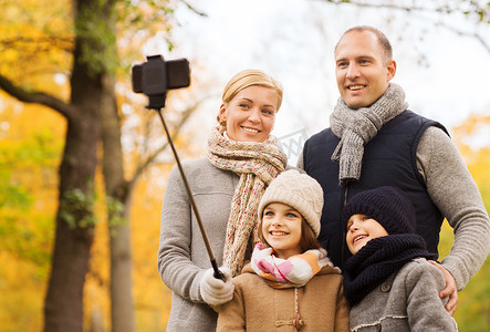 独脚架摄影照片_公园里有智能手机和独脚架的幸福家庭