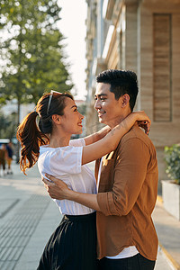 一对年轻夫妇在目的地城市拥抱的后视图，同时站在户外一家高档鞋店附近的购物区