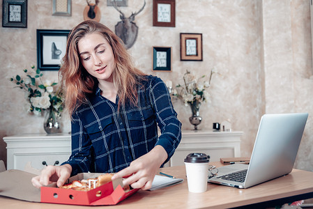 忙碌的女商人在家工作，一边在笔记本电脑桌上工作一边吃披萨，女商人在家工作，认真地沟通忙碌的任务。