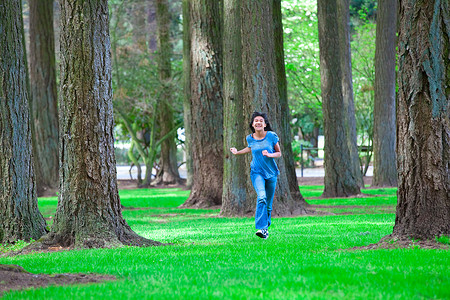 绿色树苗条摄影照片_走在高大的树下的年轻混血女孩
