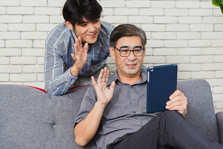 父亲和他的儿子坐在沙发上聊天视频通话