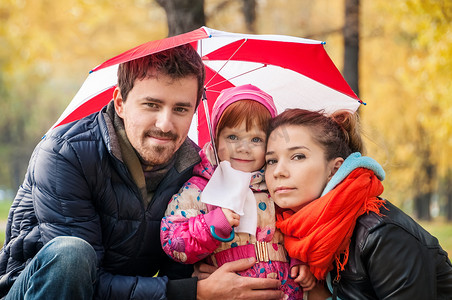 秋季公园伞下快乐的年轻家庭