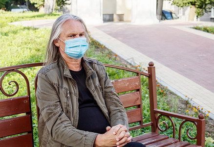老人流感摄影照片_戴防护面具的老人坐在城市公园的长凳上