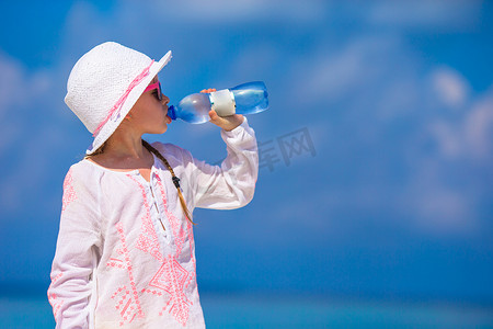 小女孩在炎热的夏日在海滩上喝矿泉水
