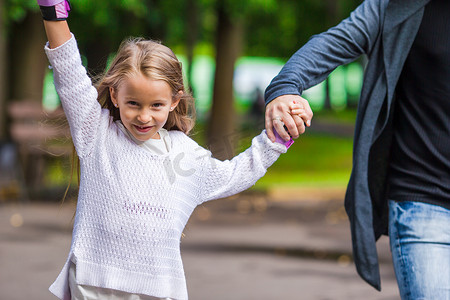 可爱的小女孩和父亲在公园里溜冰