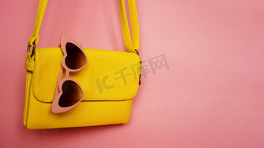 粉红色背景中的黄色包和心形太阳镜