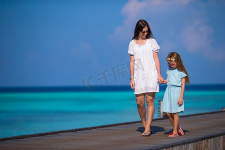 在异国情调的度假胜地的木码头上行走的小女孩和年轻母亲