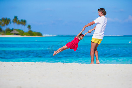 家庭度假摄影照片_热带海滩度假期间可爱的小女孩和爸爸