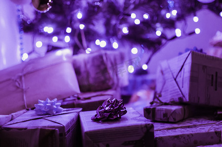 装在盒子里并用带有蝴蝶结的节日纸包裹的礼物躺在一棵圣诞树下，在 LED 花环的霓虹灯下。