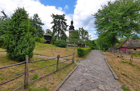 树下的石头摄影照片_在一座古老的木制教堂的背景下，一条步行道两旁排着一块大石头