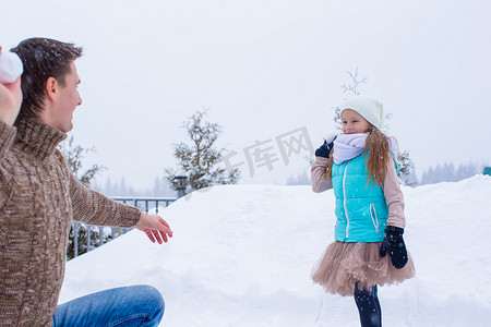 快乐的父亲和小女孩在冬天的雪天玩雪球