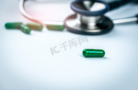 在模糊的听诊器和绿色胶囊药物背景下选择性地关注绿色胶囊药丸。
