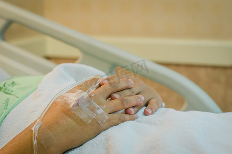 生理盐水摄影照片_躺在医院病床上接受生理盐水的男性病人的手。