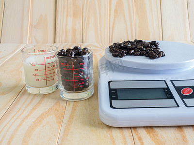 测量杯摄影照片_木板上的咖啡豆、鲜奶量杯和数字天平