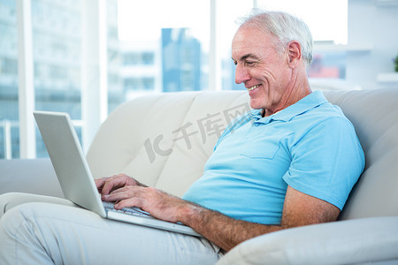 快乐的老人坐在沙发上使用笔记本电脑