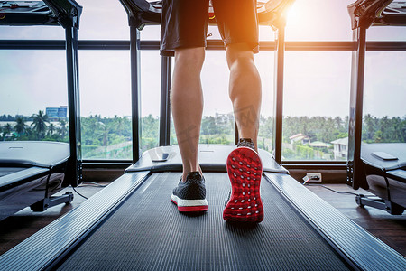 穿着运动鞋的男性脚在健身房的跑步机上跑步。