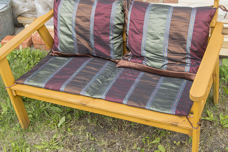 阳光明媚的夏日，花园的草地上放着一把手工制作的木椅，上面铺着纺织毯和勃艮第枕头