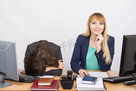 办公室里的情况——沮丧的女人躺在桌子上，她的同事高兴地看着相框