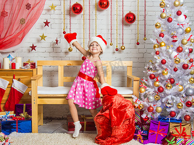 戴着帽子和圣诞老人​​手套的女孩拿着圣诞礼物围着包跳舞