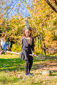 快乐的小女孩带着扫帚在万圣节穿着女巫服装。