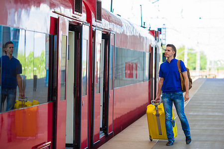 带铁轨的火车摄影照片_年轻的白人男子带着行李在车站乘火车旅行