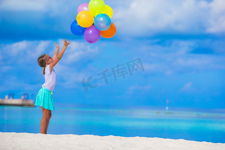 在热带海滩玩彩色气球的可爱小女孩