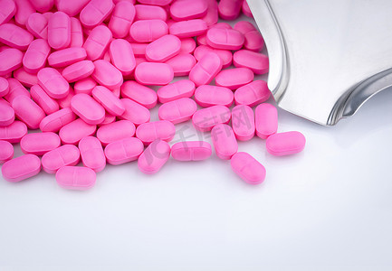 在不锈钢药物托盘附近的白色背景上的一堆粉红色药丸。