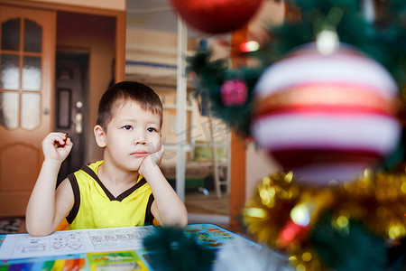 写下摄影照片_梦幻般的小男孩坐在背景圣诞树上写下他的愿望清单。