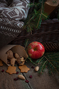 圣诞树树枝上的红黄苹果，靠近篮子，上面放着羊毛衫和一本旧书
