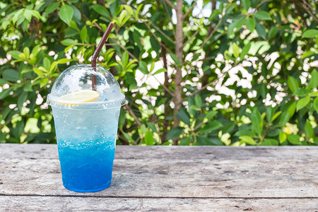 名仁苏打水摄影照片_绿叶背景木桌上的蓝色柠檬苏打，自然清新
