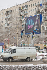 街头贴纸摄影照片_广告公司的员工在街头广告牌“夜间促销”上张贴横幅