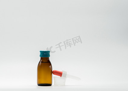 琥珀瓶中的药糖浆，带有空白标签和塑料量杯，白色背景中的茶匙