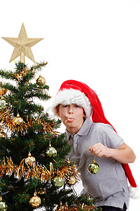 戴着圣诞帽的男孩在圣诞树上伸出舌头