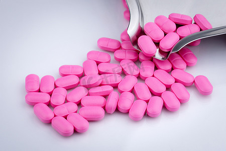 在不锈钢药物托盘附近的白色背景上的一堆粉红色药丸。