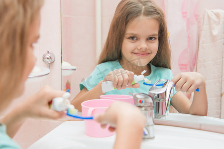 挤牛奶摄影照片_六岁女孩从牙刷上的管子里挤牙膏