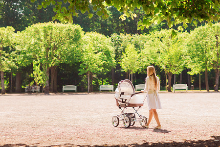 妈妈推孩子摄影照片_公园里推着婴儿车的快乐妈妈