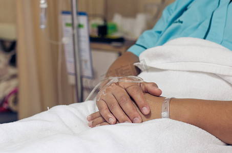 躺在医院病床上接受生理盐水的男性病人的手。
