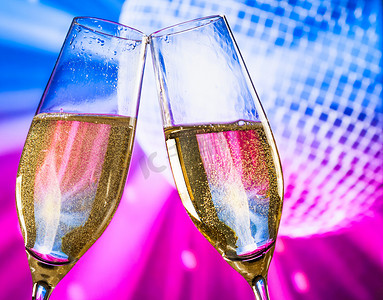 紫色气泡饮料摄影照片_带有金色气泡的香槟杯在闪闪发光的蓝色和紫色迪斯科舞会背景上欢呼