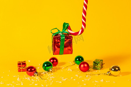 糖果手杖棒棒糖拿着一个礼盒，里面有黄色背景的圣诞礼物，圣诞糖果和新年装饰